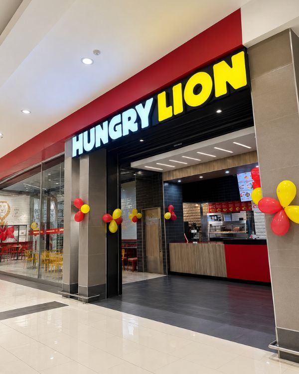 Completed Hungry Lion Takeaway Franchise Fit-Out Polished storefront view of a completed Hungry Lion takeaway franchise inside a shopping mall, showing the illuminated signage, entrance, service counter, branded interior finishes, and red and yellow opening décor.