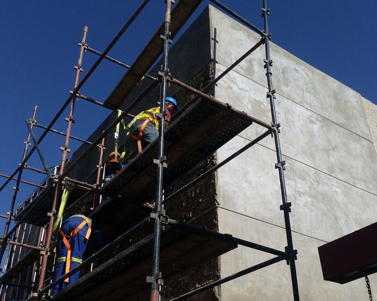 Construction workers on scaffold performing façade repair and structural surface restoration on a commercial building exterior in South Africa